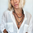 Woman wearing a white shirt and multiple necklaces against a plain background