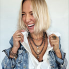Woman wearing a denim jacket and layered necklaces against a white background