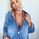 Woman wearing a blue denim shirt and red beaded necklace against a plain background
