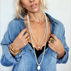 Woman wearing a denim jacket with a pearl necklace and gold jewelry against a white background