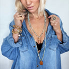 Woman wearing a blue denim shirt with layered necklaces and bracelets against a white background