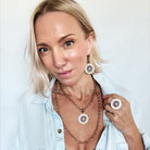 Woman wearing a light blue denim jacket with layered necklaces and earrings.