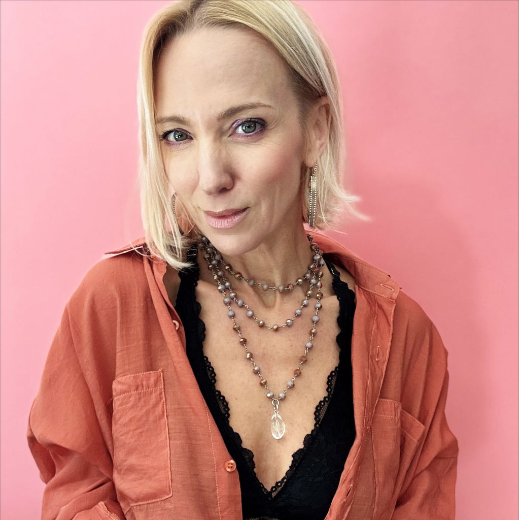 A stylish multi-layered necklace featuring delicate rosary-style chains adorned with small beads and intricate silver accents. The necklace includes multiple strands of varying lengths, with the longest featuring a teardrop-shaped pendant. The design combines bohemian and vintage aesthetics, complementing the wearer's black lace top and earthy-toned outfit.