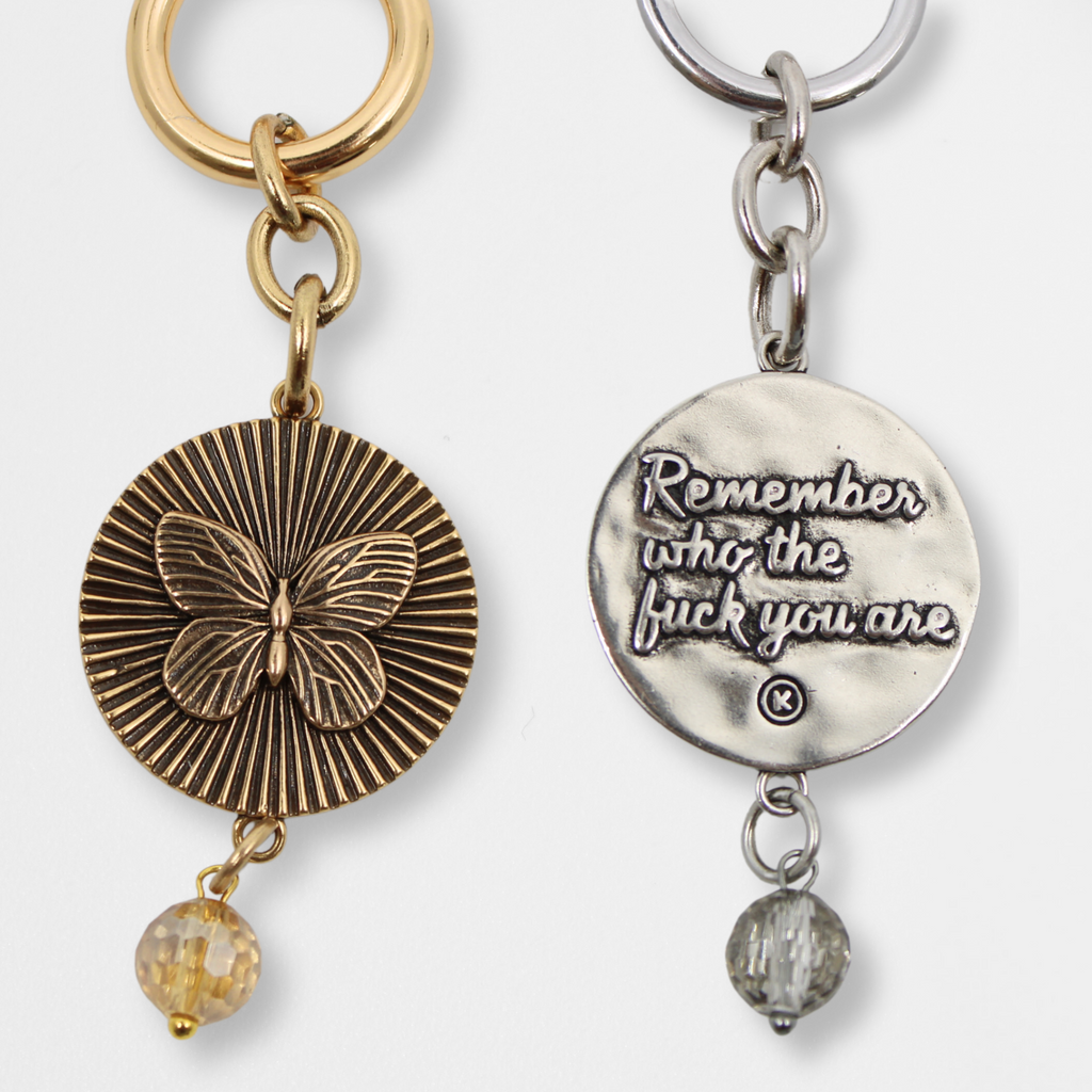 COVER IMAGE OF FRONT AND BACK MESSAGE AND GOLD AND SILVER FINISH; Two VIEWS: one with a butterfly pendant and crystal accent, the other boldly inscribed with Remember who the fuck you are.