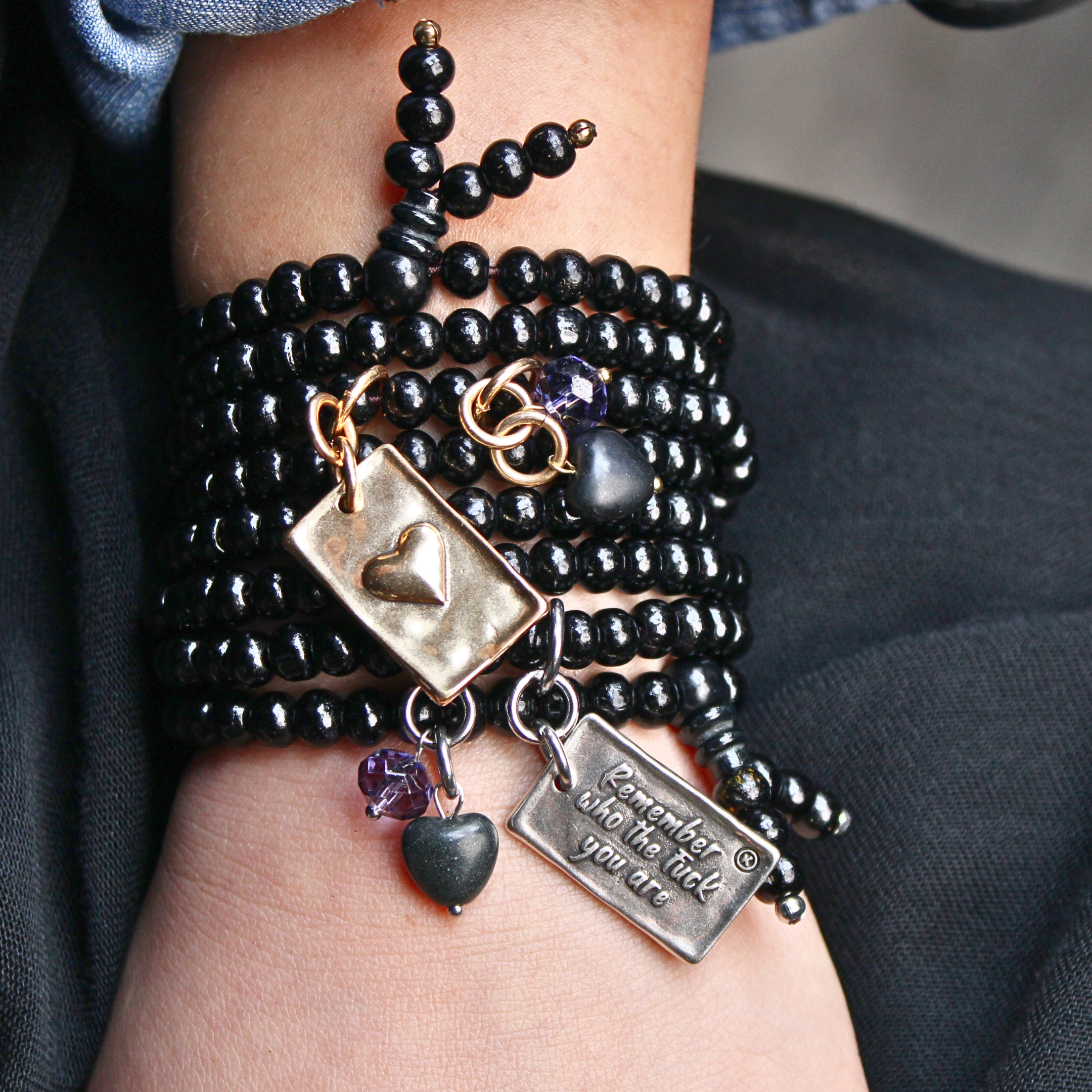 Black beaded bracelet with charms on a wrist against a dark background
