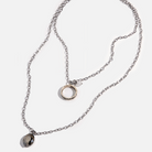 A collection of jewelry including a silver ring with an inscription, a gold necklace with a clear faceted crystal and a rose quartz heart accent, and a silver necklace with a faceted smoky crystal and moonstone accent.