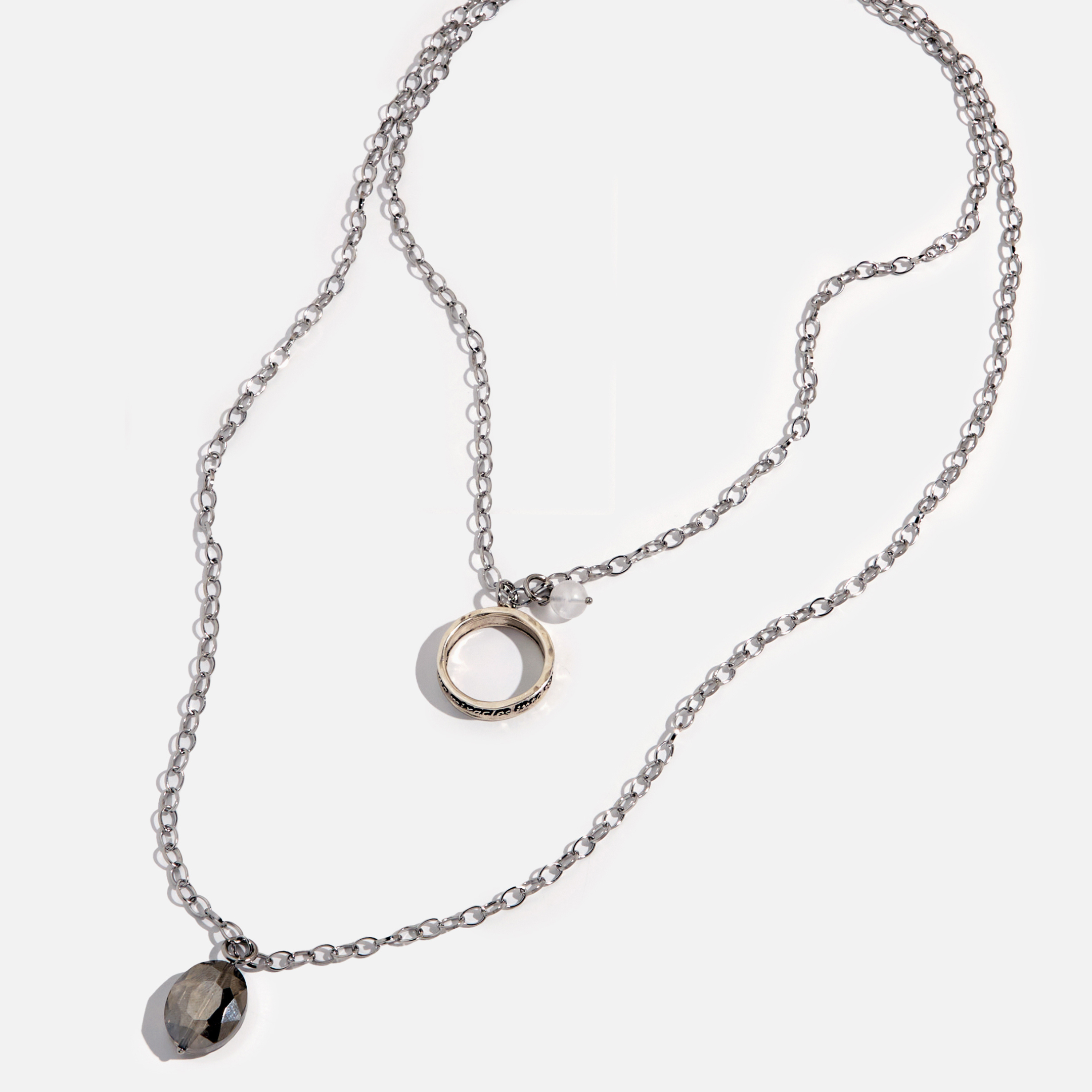 A collection of jewelry including a silver ring with an inscription, a gold necklace with a clear faceted crystal and a rose quartz heart accent, and a silver necklace with a faceted smoky crystal and moonstone accent.