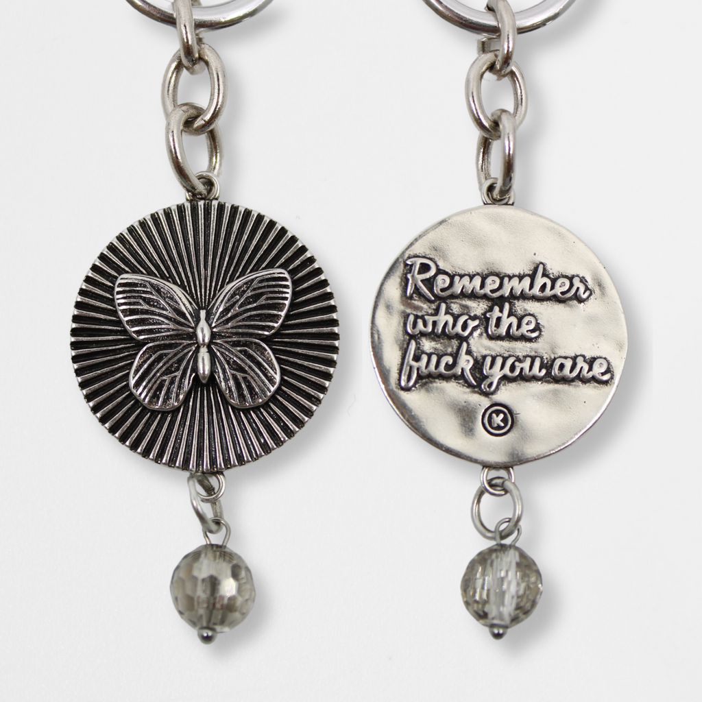 DETAILS AND PRODUCT DISPLAY OF SILVER VARIANT; one with a butterfly pendant and crystal accent, the other boldly inscribed with Remember who the fuck you are.