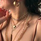 Close-up of layered necklaces and a gold hoop earring on a person.