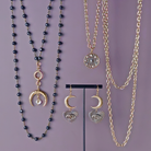 Jewelry set with black beaded necklace, gold chain, and earrings on a purple background