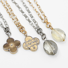 Two necklaces side by side, one with a gold chain and clover pendant, and the other with a silver chain and smoky crystal pendant.