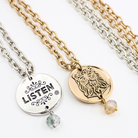 Two chain necklaces with round pendants: one silver with LISTEN adorned in plated brass and small beads, the other gold featuring a face design. Each piece exudes charm, enhanced by subtle crystal accents.