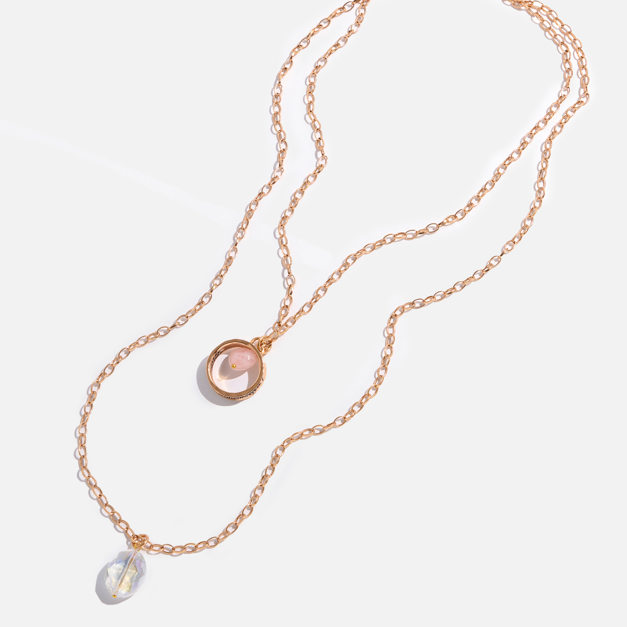 A collection of jewelry including a silver ring with an inscription, a gold necklace with a clear faceted crystal and a rose quartz heart accent, and a silver necklace with a faceted smoky crystal and moonstone accent.