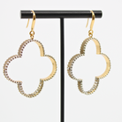 A pair of gold-colored composite drop earrings with French ear wire, featuring a clover design with a message inscribed inside, displayed on an earing stand.