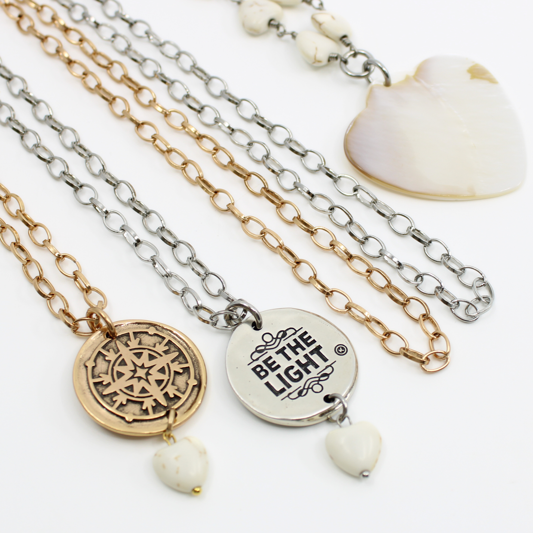 Two layered necklaces, one with a gold-tone compass pendant and the other with a silver-tone pendant, both accompanied by white howlite heart beads on a chain.