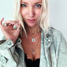 Woman wearing a light green jacket and layered necklaces with a neutral background