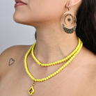 Woman wearing a yellow beaded necklace and earrings on a plain background