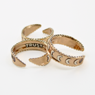 Three mixed-metal rings with crescent moon designs and TRUST engraved inside, each featuring adjustable bands, are shown from different angles.