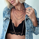 Person wearing multiple necklaces and a ring with a denim jacket on a light blue background