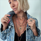 Woman wearing layered necklaces and rings with a denim jacket on a light background