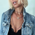 Woman wearing a denim jacket and layered necklaces with a light blue background