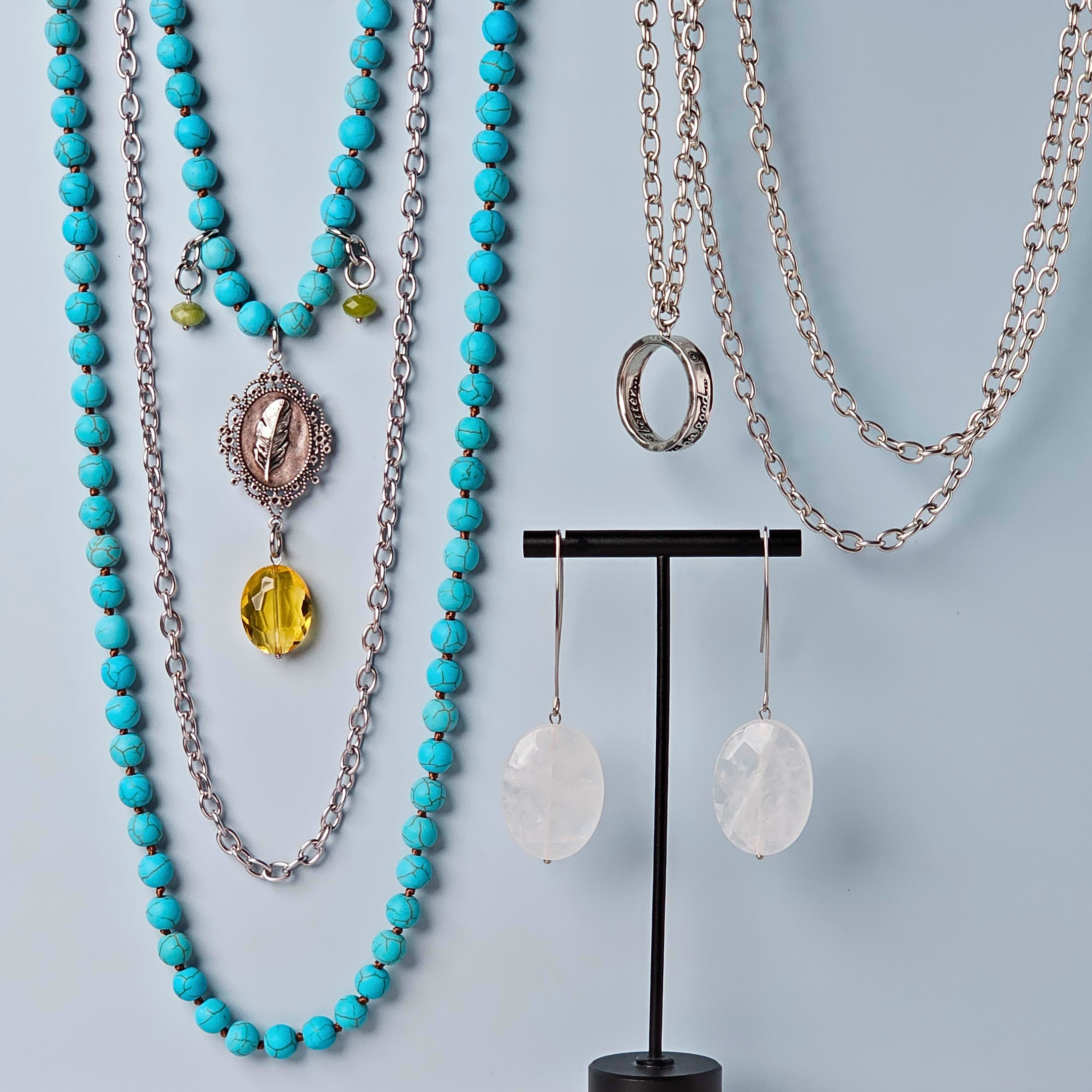 Jewelry set with turquoise beaded necklace, silver chain, and earrings on a light blue background