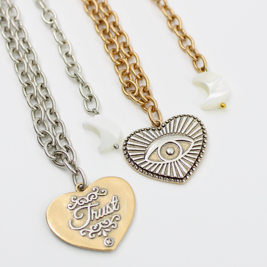 Gold chain choker with a heart-shaped eye pendant, bar clasp, and crescent moon charm. Its mixed metal design adds a unique flair, all set against a white background.