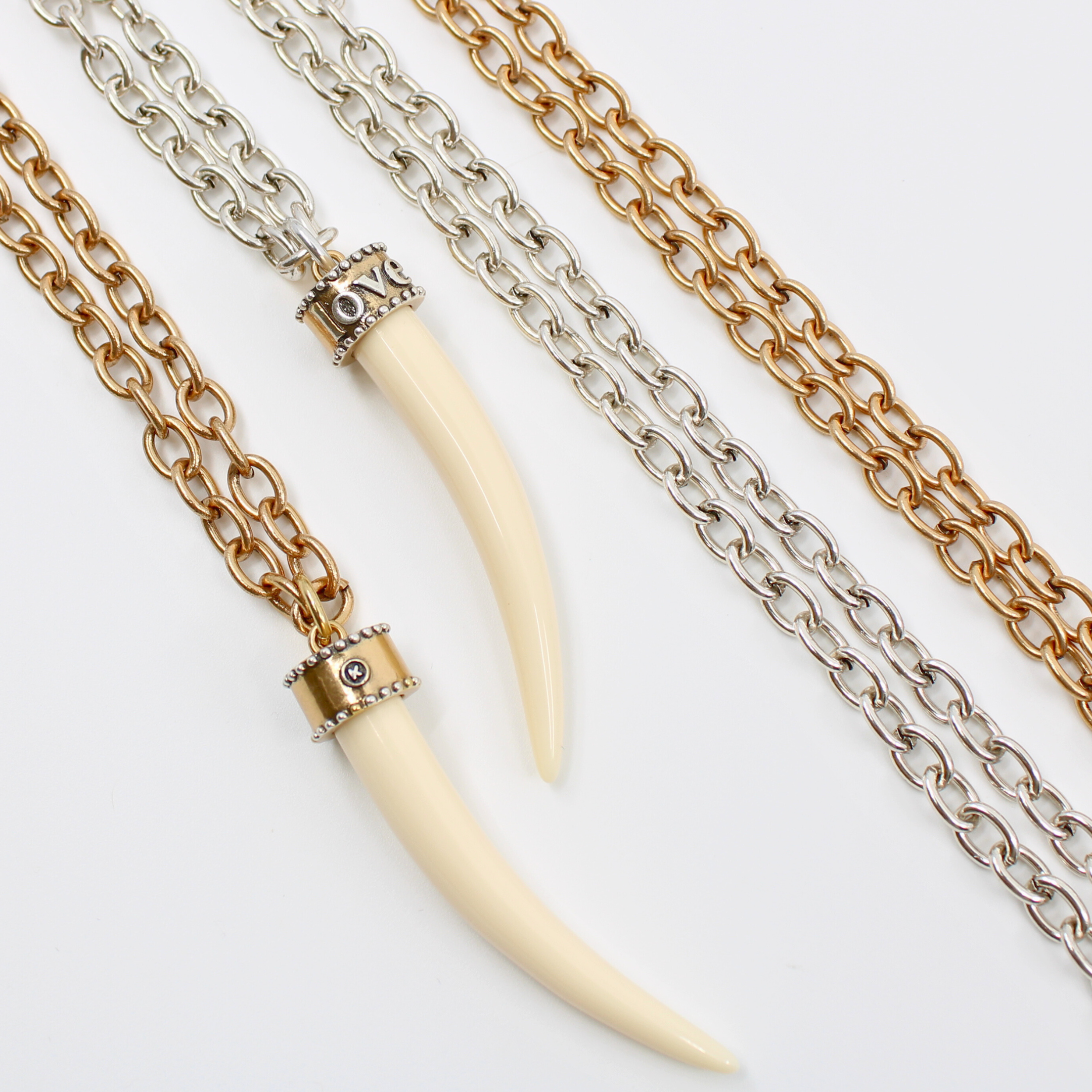 Two tusk-shaped pendants, crafted from synthetic polymer, hang gracefully from mixed metal design chain necklaces of silver and bronze, displayed side by side on a white background.