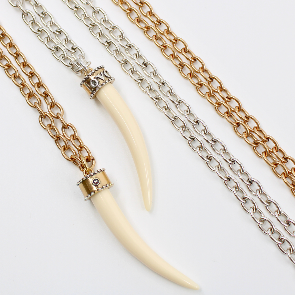 Two tusk-shaped pendants, crafted from synthetic polymer, hang gracefully from mixed metal design chain necklaces of silver and bronze, displayed side by side on a white background.