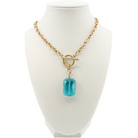 Gold necklace with a blue pendant on a white mannequin bust.
