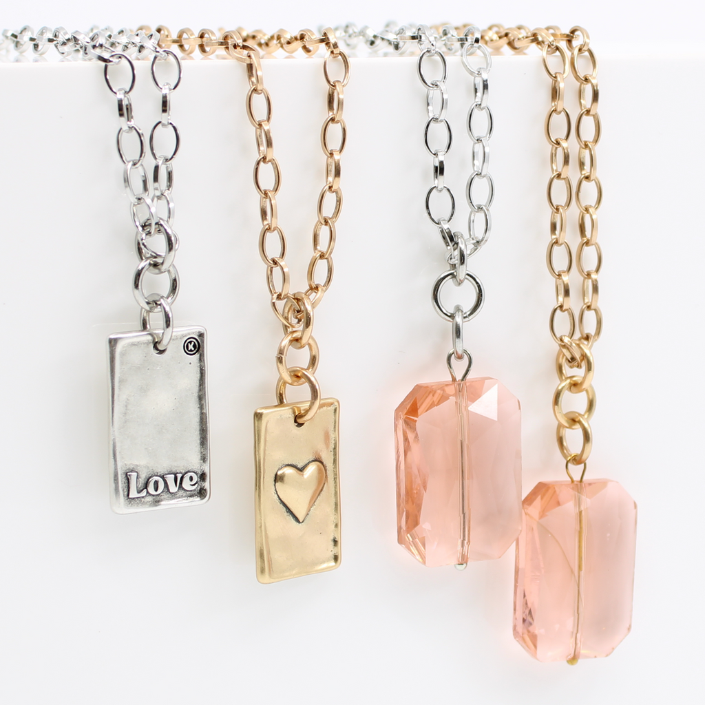 A black jewelry display showcases two elegant chain necklaces: one features a peach crystal stone pendant, while the other flaunts a gold LOVE pendant. Separate close-ups capture the intricate beauty of both pendants.