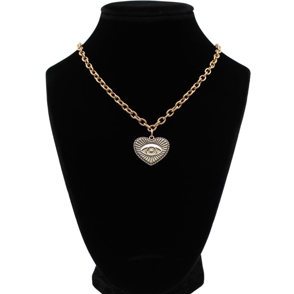 Gold chain choker with a heart-shaped eye pendant, bar clasp, and crescent moon charm. Its mixed metal design adds a unique flair, all set against a white background.