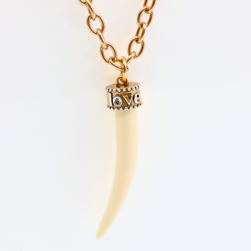 gold chain & tusk-shaped pendant, crafted from synthetic polymer, hang gracefully from gold chain necklace, displayed on a white background.