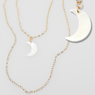 Two gold necklaces with white crescent moon pendants on a light gray background