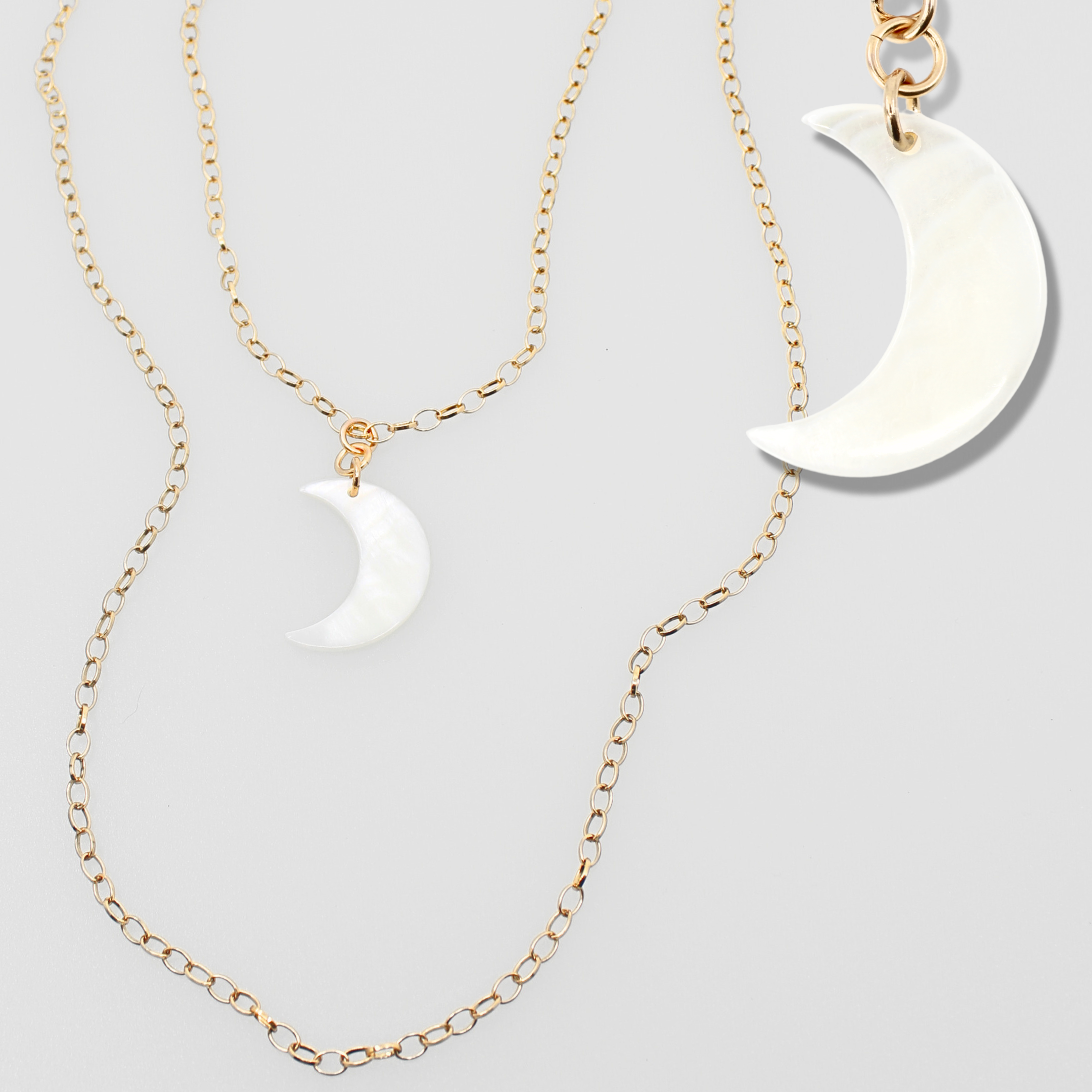 Two gold necklaces with white crescent moon pendants on a light gray background