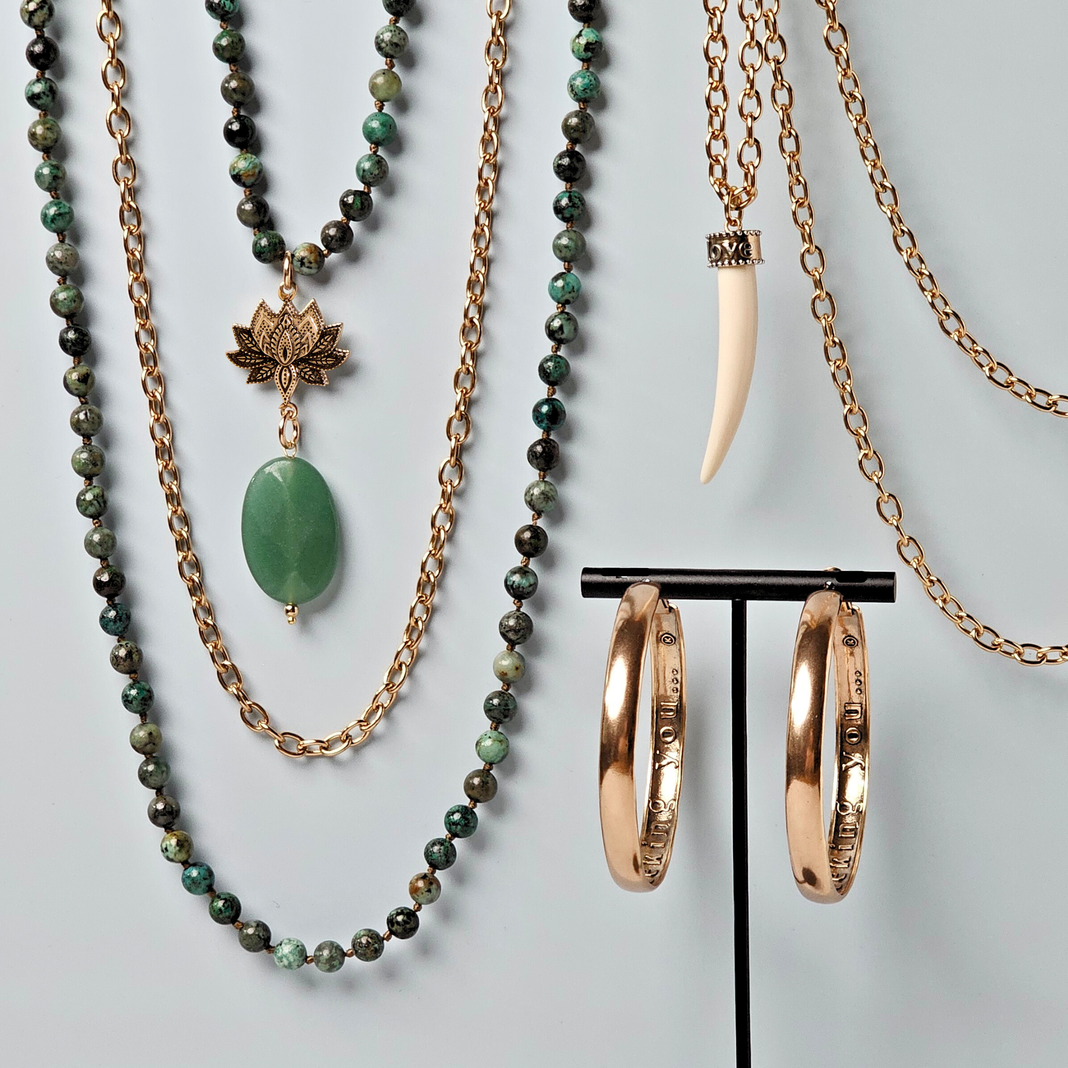 Jewelry set with green beaded necklaces and gold hoop earrings on a gray background