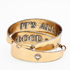 A pair of two-toned hoop earrings with intricate detailing. The outer surface features small, engraved sunburst designs with a tiny central accent. The edges of the hoops have a textured trim, adding to a vintage-inspired boho aesthetic. The inner band of the hoops is inscribed with raised lettering with the message "It's All Good." The earrings have a polished gold finish, giving them a stylish and elegant look.