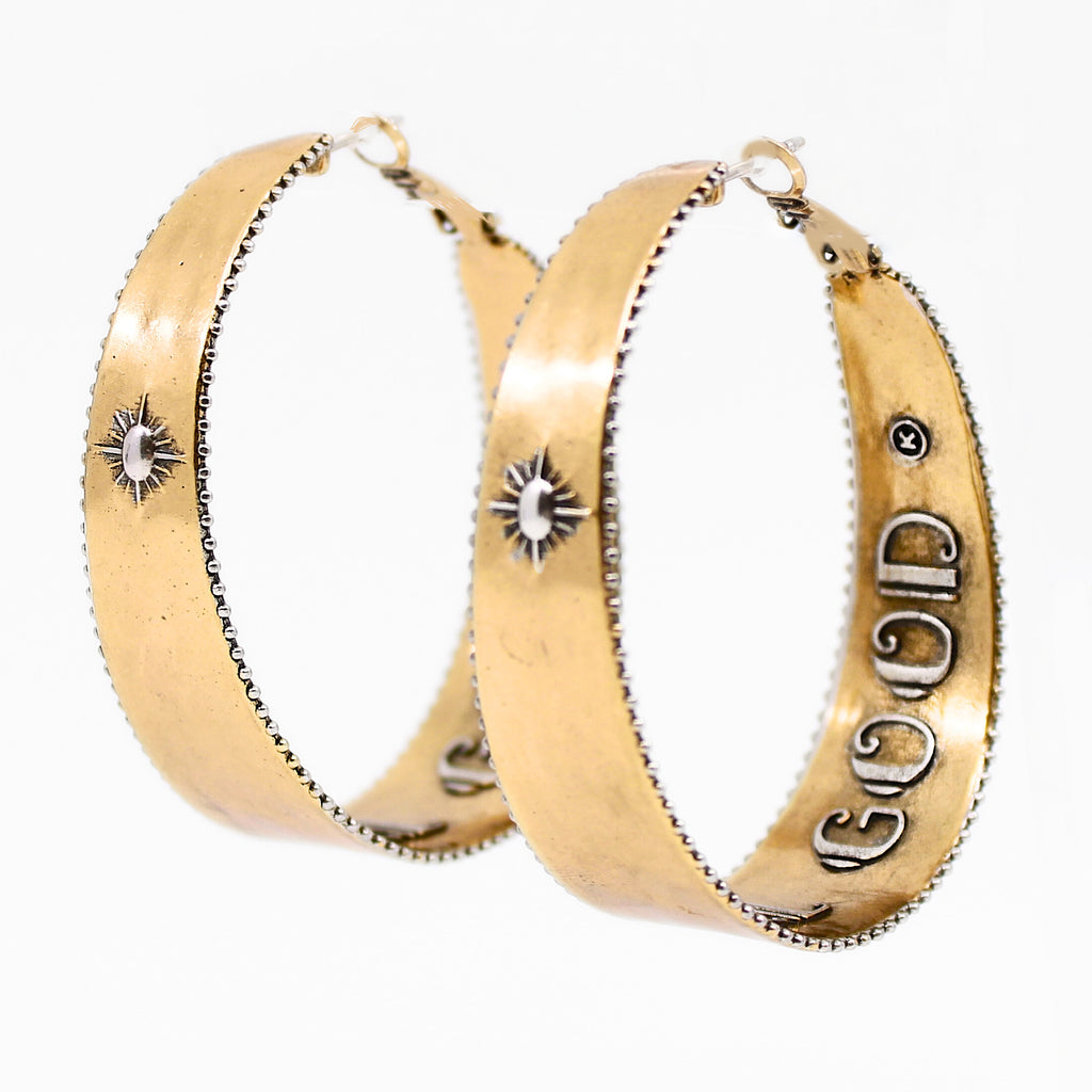 A pair of two-toned hoop earrings with intricate detailing. The outer surface features small, engraved sunburst designs with a tiny central accent. The edges of the hoops have a textured trim, adding to a vintage-inspired boho aesthetic. The inner band of the hoops is inscribed with raised lettering with the message "It's All Good." The earrings have a polished gold finish, giving them a stylish and elegant look.