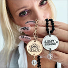 A person showcasing a necklace with a gold-toned pendant engraved with a lotus flower and the phrase 'JUST BREATHE', accompanied by a chain with beaded crystals.