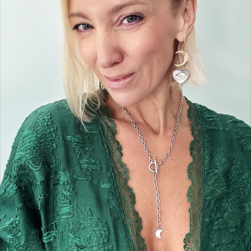 model wearing chain choker with a heart-shaped eye pendant, bar clasp, and crescent moon charm. Its mixed metal design adds a unique flair, all set against a white background.