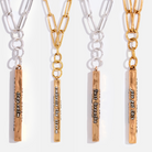 A collection of four 'Stay Calm' Klink necklaces, featuring plated brass paperclip chains and antique gold finish vertical bar pendants with messages on each side. Each necklace has a different length.