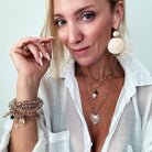 A person wearing a white shirt, showcasing multiple pieces of jewelry including a heart-shaped pendant necklace, a chain necklace with a faceted crystal accent, and several bracelets on the wrist.