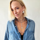 Woman wearing a blue denim shirt with layered necklaces against a plain background