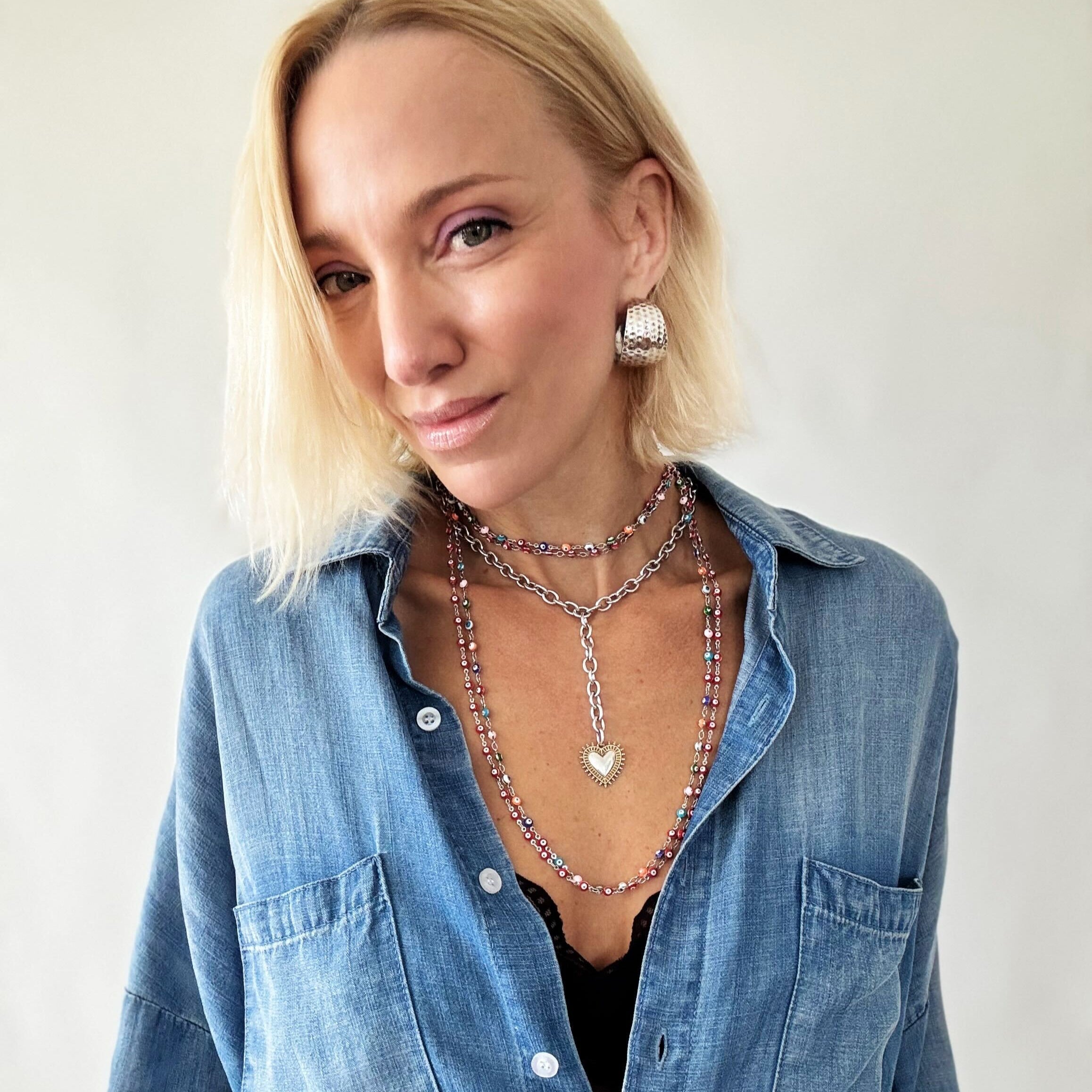 Woman wearing a blue denim shirt with layered necklaces against a plain background