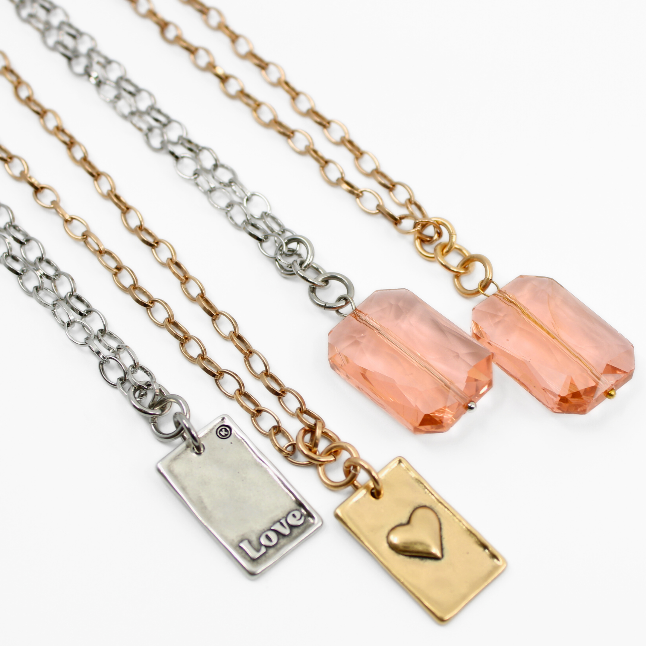 A jewelry display showcases two views of an elegant chain necklace: both feature a peach crystal stone pendant, while the other flaunts the gold LOVE pendant. Separate close-ups capture the intricate beauty of both pendants.