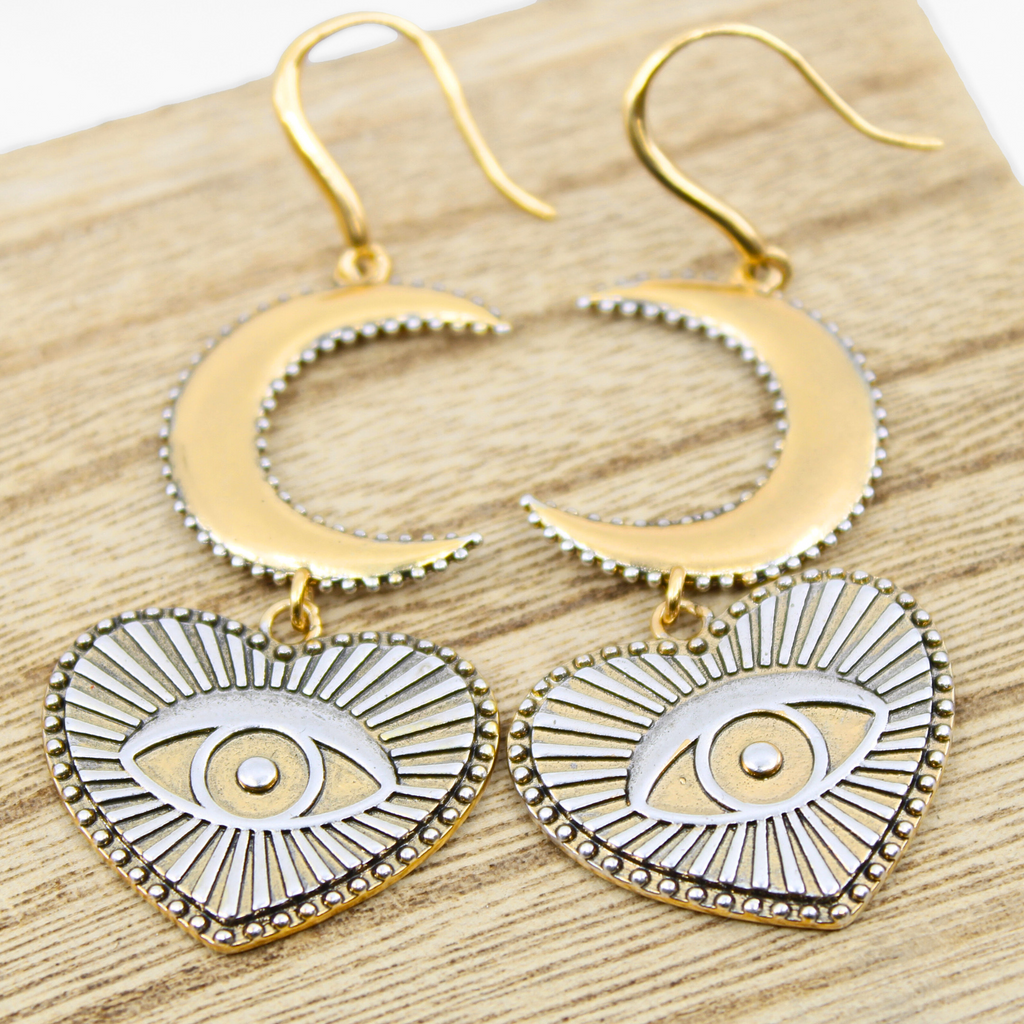 Gold earrings with crescent moons and heart-shaped pendants featuring eye designs, crafted in a mixed metal design. The pieces elegantly suspend from French ear wires, creating a captivating composite drop earring effect.