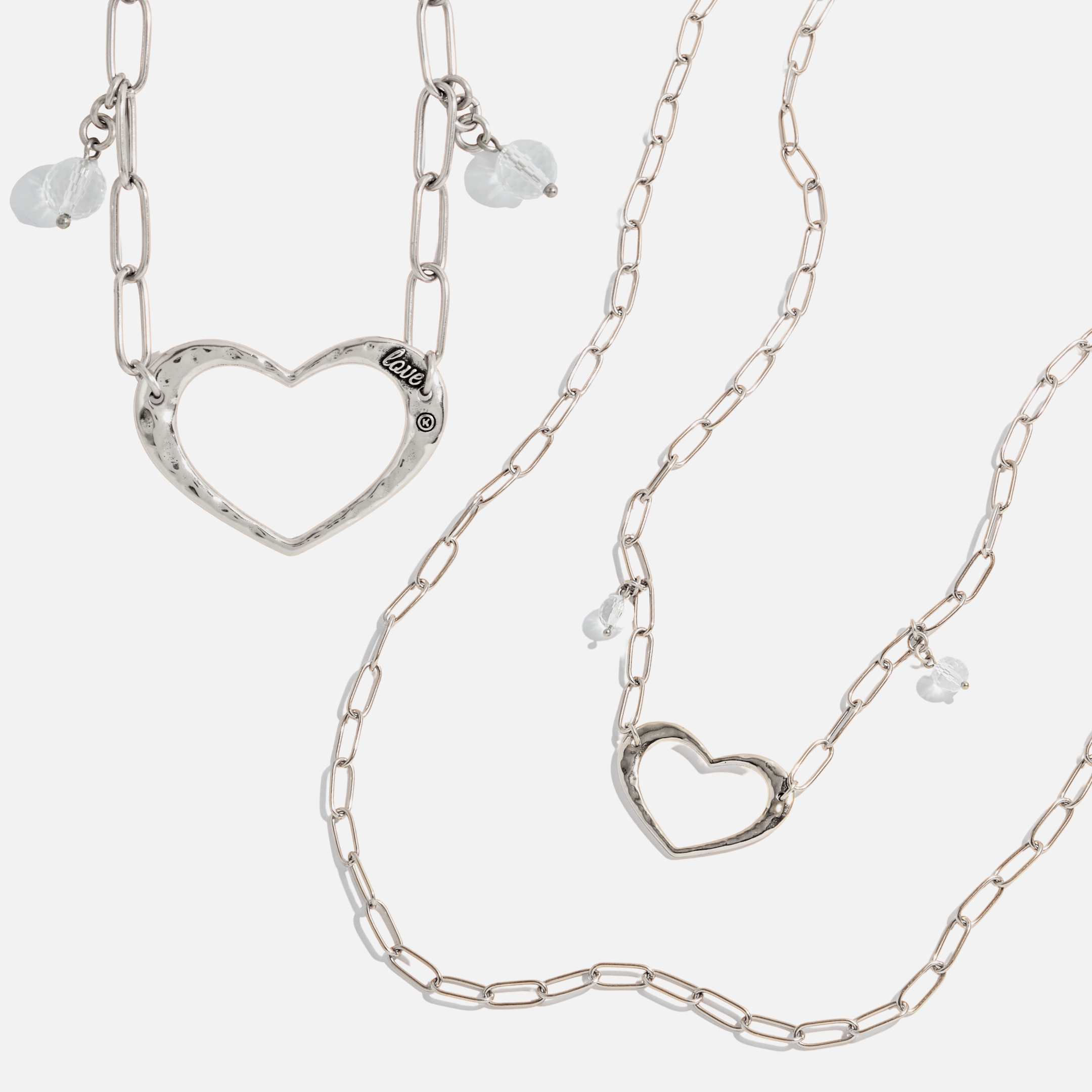 Two long chain necklaces with open heart pendants and crystal quartz accents, one with a gold-tone heart and clear quartz, and the other with a silver-tone heart and clear quartz.