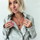 Woman wearing a gray jacket with jewelry, including a necklace and ring, on a light background.