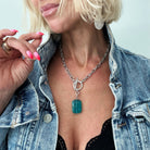 Woman wearing a denim jacket with a necklace featuring a blue pendant.