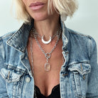 Person wearing a denim jacket with layered necklaces featuring a moon symbol and clear pendant.
